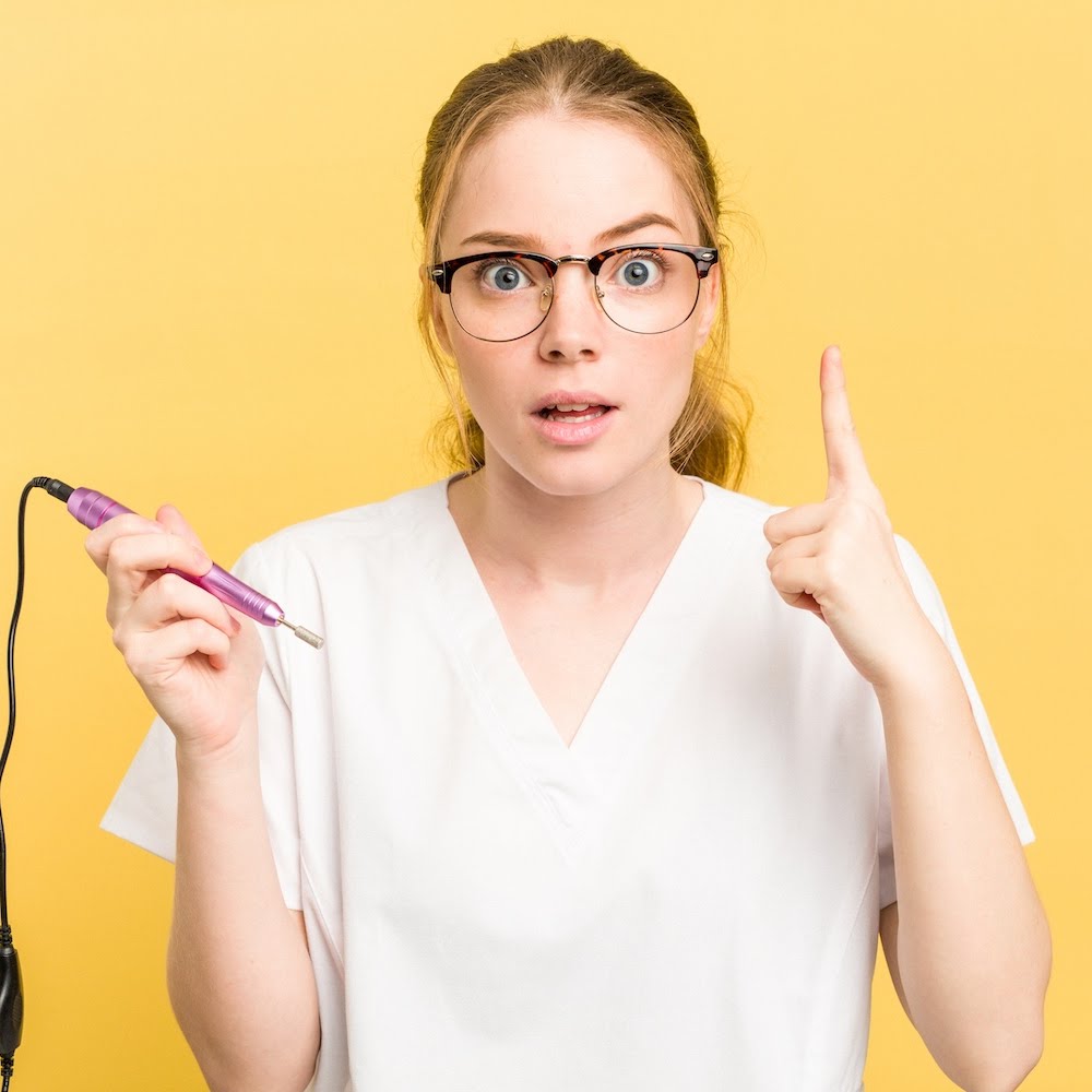 Surprised nail technician holding an electric nail file against a yellow background